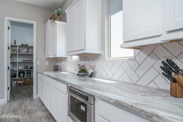 kitchen with light stone counters, backsplash, light hardwood / wood-style floors, and white cabinets