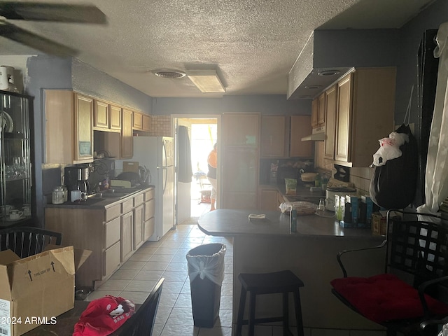 kitchen featuring a textured ceiling, light brown cabinetry, white fridge, and sink