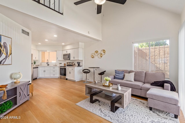 living area featuring visible vents, a towering ceiling, ceiling fan, light wood-style floors, and recessed lighting