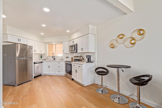 kitchen with light wood finished floors, white cabinetry, stainless steel appliances, and light countertops