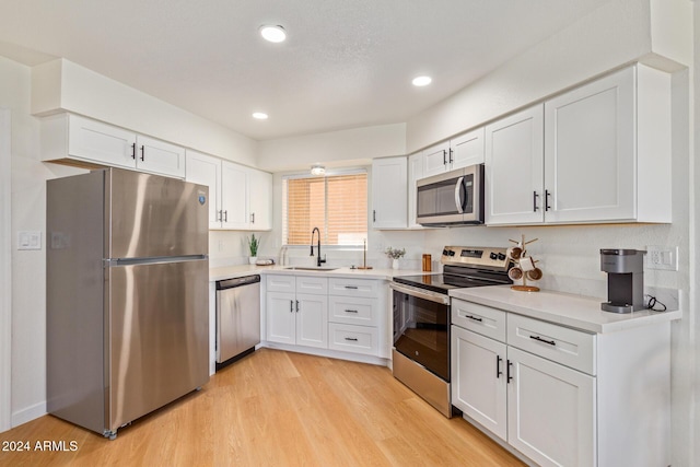 kitchen with white cabinets, appliances with stainless steel finishes, light countertops, light wood-type flooring, and a sink