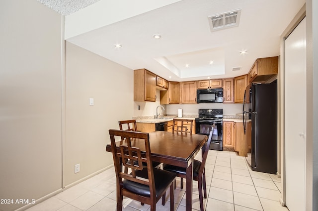 kitchen with a tray ceiling, sink, light tile patterned floors, and black appliances