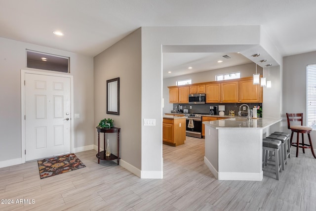 kitchen featuring kitchen peninsula, stainless steel appliances, sink, pendant lighting, and a breakfast bar area