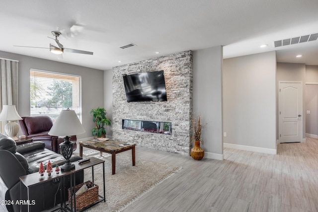 living room with light hardwood / wood-style floors, a stone fireplace, and ceiling fan