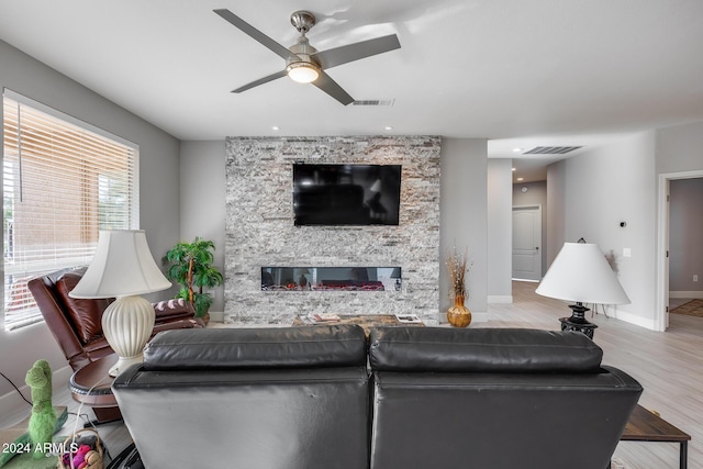 living room with a stone fireplace, ceiling fan, and light hardwood / wood-style flooring