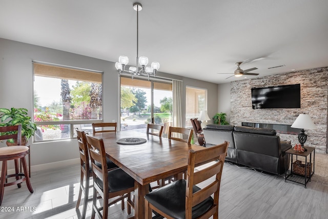 dining room featuring ceiling fan with notable chandelier and a stone fireplace