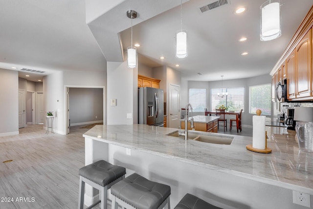 kitchen featuring sink, hanging light fixtures, stainless steel fridge, light hardwood / wood-style floors, and kitchen peninsula