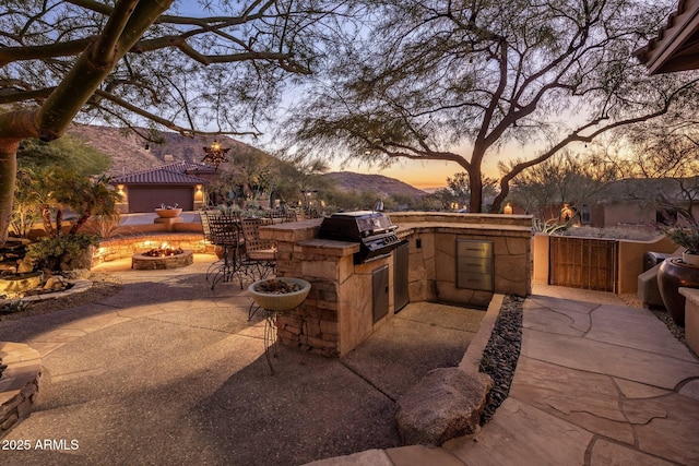 view of patio / terrace with exterior kitchen, a fire pit, fence, and a grill