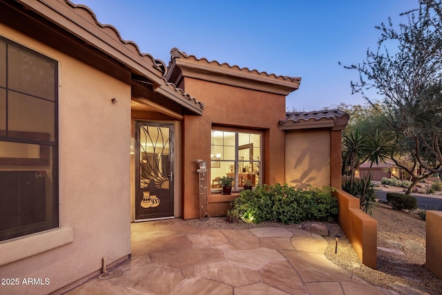 property entrance with a tiled roof, stucco siding, and a patio area