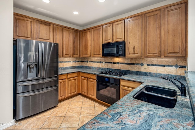 kitchen with light tile patterned floors, decorative backsplash, brown cabinetry, black appliances, and a sink