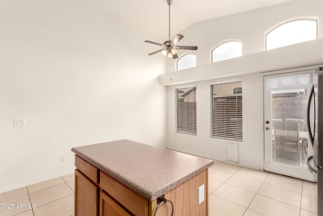 kitchen with high vaulted ceiling, a kitchen island, light tile patterned flooring, freestanding refrigerator, and ceiling fan