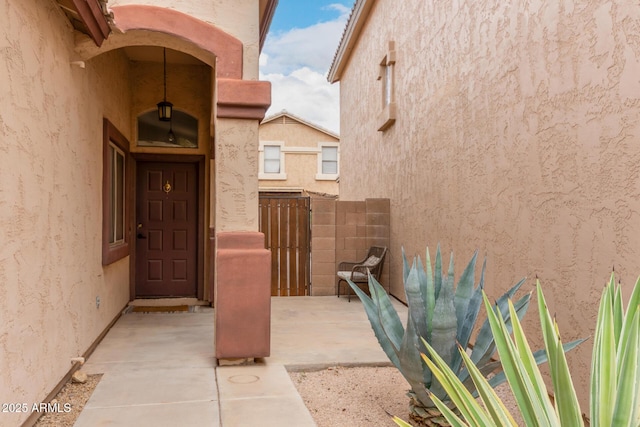 view of exterior entry with stucco siding and fence