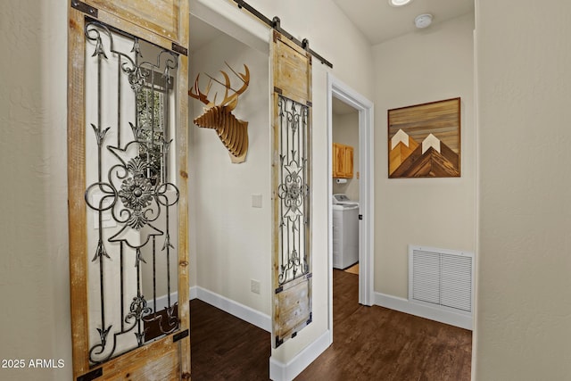 hall featuring washer / clothes dryer, dark hardwood / wood-style floors, and a barn door