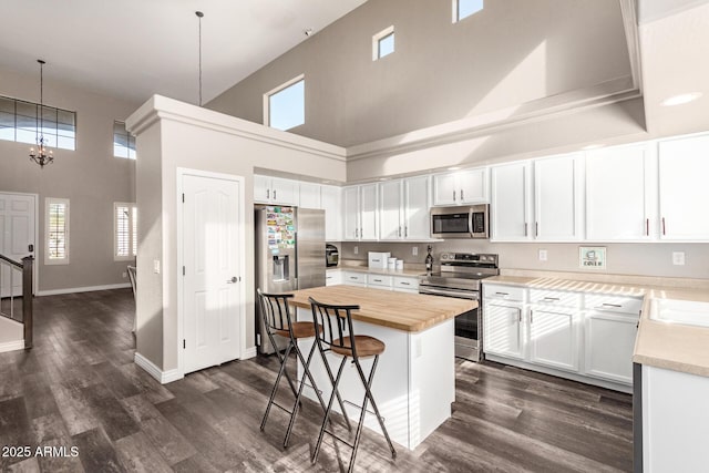 kitchen with a kitchen bar, appliances with stainless steel finishes, a towering ceiling, decorative light fixtures, and white cabinets