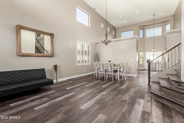 dining room with a towering ceiling, dark wood-type flooring, a wealth of natural light, and an inviting chandelier