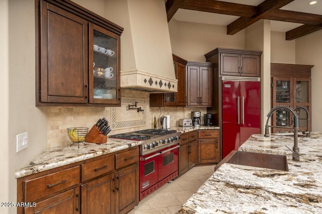 kitchen featuring sink, range with two ovens, built in refrigerator, custom range hood, and decorative backsplash