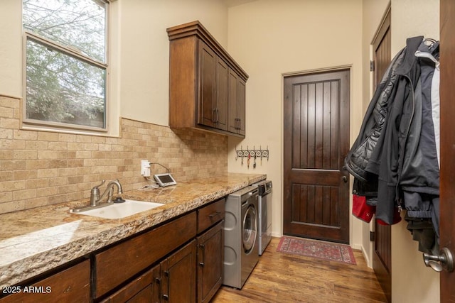 clothes washing area with cabinets, sink, washing machine and dryer, and light hardwood / wood-style flooring