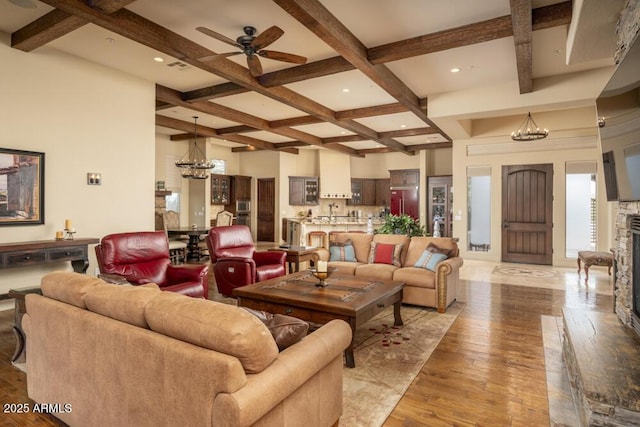 living room with ceiling fan with notable chandelier, a fireplace, beamed ceiling, coffered ceiling, and light wood-type flooring