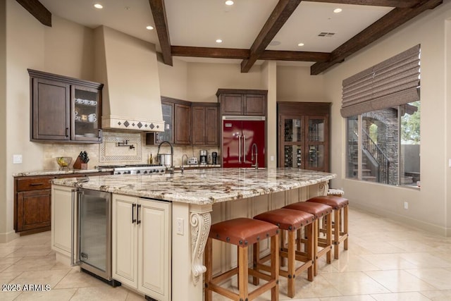 kitchen featuring a spacious island, wine cooler, custom exhaust hood, built in fridge, and light stone countertops