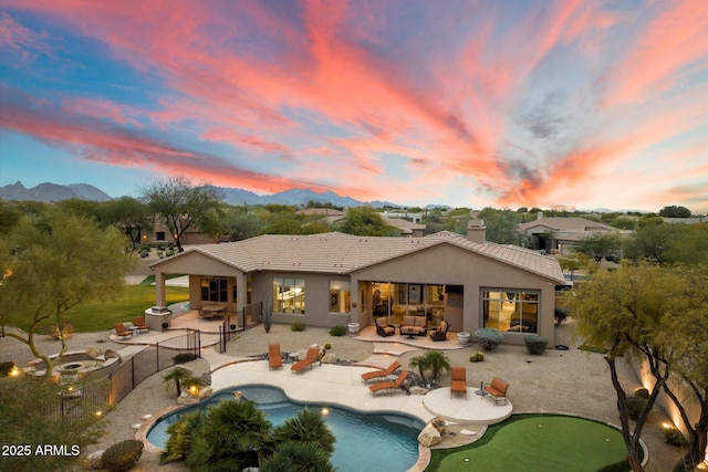 back house at dusk featuring a mountain view, a patio, and a fenced in pool