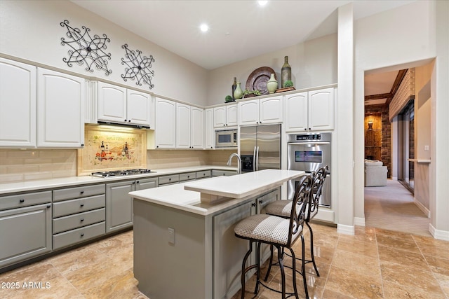 kitchen with a breakfast bar, white cabinetry, gray cabinetry, a kitchen island with sink, and stainless steel appliances