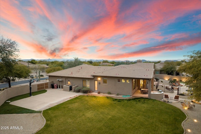 back house at dusk featuring a patio area and a lawn