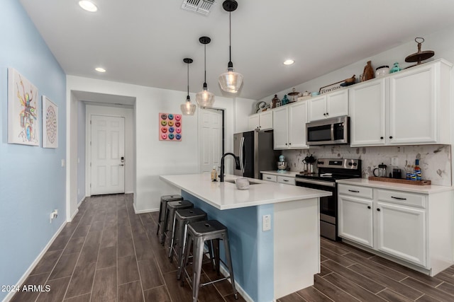 kitchen featuring a center island with sink, decorative light fixtures, white cabinets, and stainless steel appliances