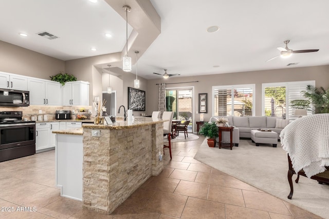 kitchen featuring pendant lighting, white cabinets, stainless steel range with electric cooktop, a kitchen island with sink, and light stone countertops