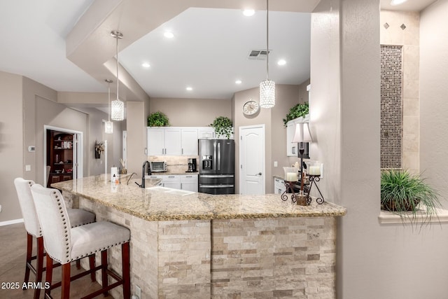 kitchen featuring sink, light stone counters, decorative light fixtures, stainless steel fridge, and white cabinets