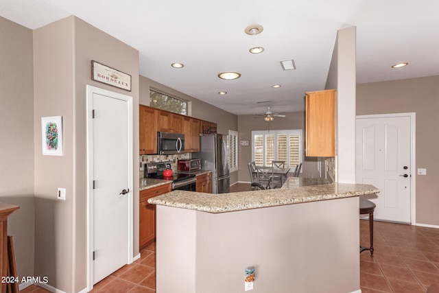 kitchen featuring ceiling fan, stainless steel appliances, light stone counters, kitchen peninsula, and a breakfast bar