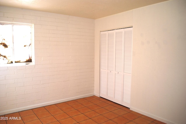 unfurnished bedroom featuring tile patterned floors, a closet, and brick wall