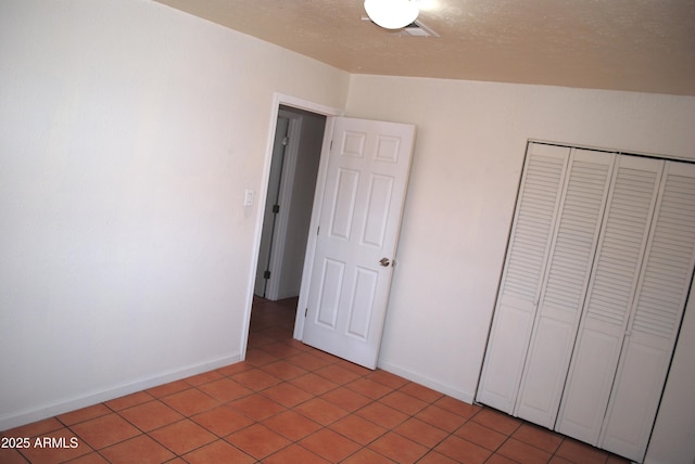 unfurnished bedroom with visible vents, a textured ceiling, a closet, light tile patterned flooring, and baseboards