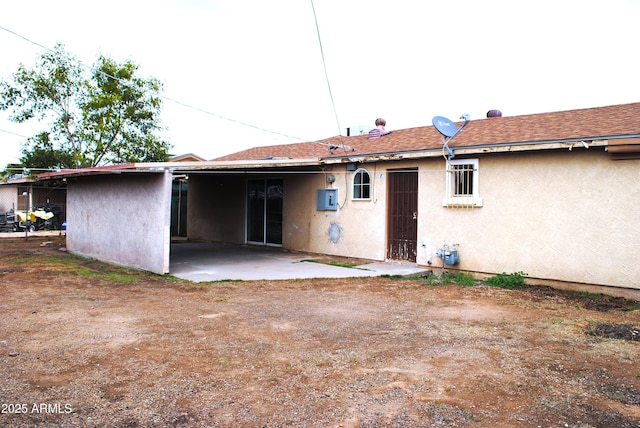 rear view of property featuring a shingled roof, a patio, a carport, and stucco siding