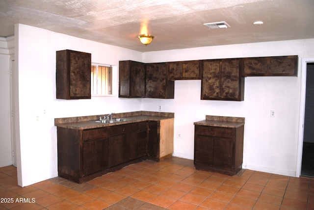 kitchen featuring visible vents, a sink, dark countertops, a textured ceiling, and dark brown cabinetry