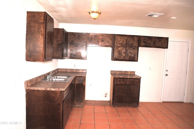 kitchen featuring light tile patterned floors, visible vents, a sink, dark brown cabinets, and dark countertops