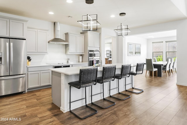 7180 W Tombstone Trl, Peoria, AZ 85383 - kitchen featuring stainless steel appliances, wall chimney range hood, a kitchen island with sink, a breakfast bar area, and light countertops
