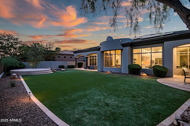 7775 E Fledgling Dr, Scottsdale, AZ 85255 - back of house at dusk with a patio, a fenced backyard, stucco siding, a chimney, and roof mounted solar panels
