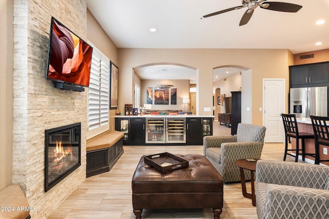 living room featuring wine cooler, ceiling fan, a fireplace, and light wood-type flooring