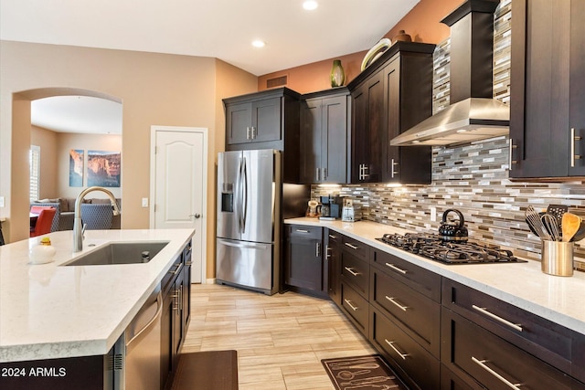 kitchen featuring a kitchen island with sink, sink, wall chimney exhaust hood, light stone counters, and stainless steel appliances