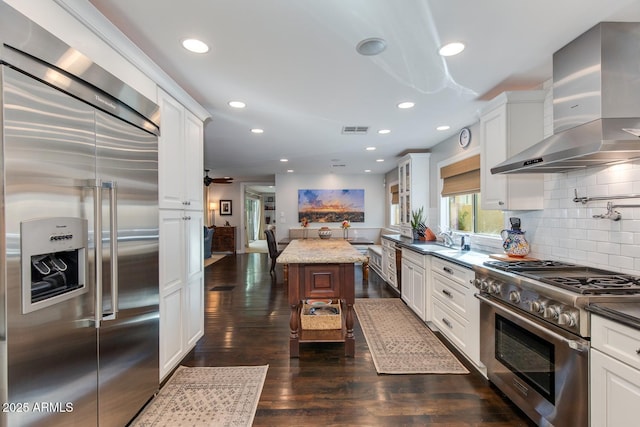 kitchen with dark wood-type flooring, backsplash, premium appliances, white cabinets, and wall chimney exhaust hood