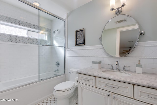 full bathroom with enclosed tub / shower combo, vanity, tile walls, and toilet