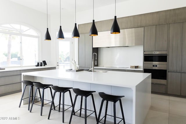 kitchen featuring sink, black electric stovetop, a kitchen bar, pendant lighting, and a center island with sink