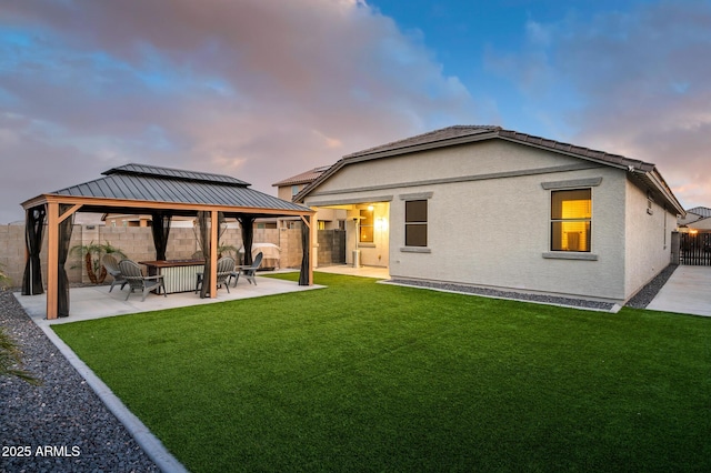 back house at dusk with a patio area, a gazebo, and a lawn