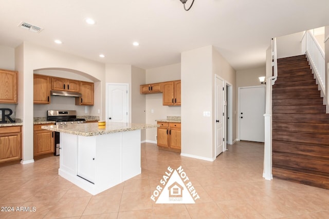 kitchen with gas stove, light stone countertops, a center island, and light tile patterned flooring