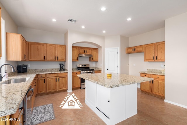 kitchen with light stone counters, a center island, sink, and stainless steel appliances