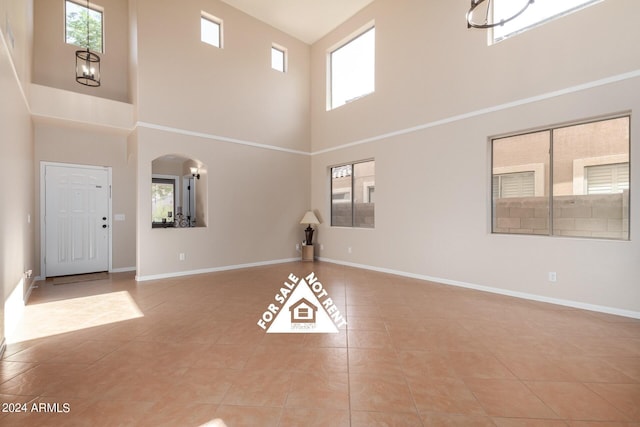 unfurnished living room featuring light tile patterned flooring, a chandelier, and a high ceiling