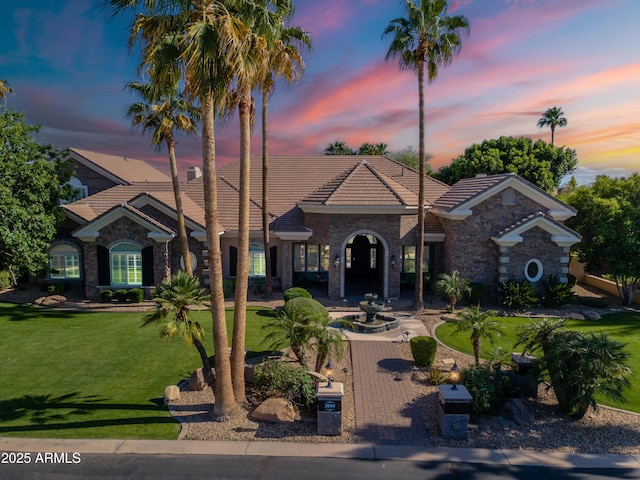 mediterranean / spanish home featuring a yard, a tiled roof, and stone siding