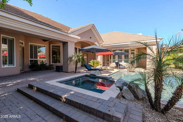 rear view of property featuring a tile roof, a patio area, an in ground hot tub, and stucco siding