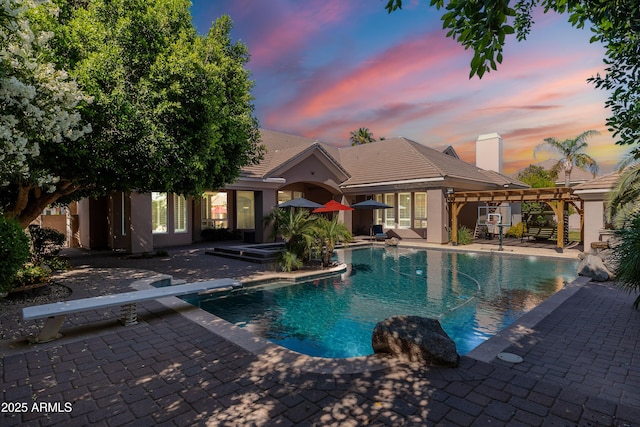 pool at dusk with a jacuzzi, a patio, an outdoor pool, and a diving board