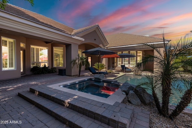 pool at dusk featuring a patio area and an in ground hot tub